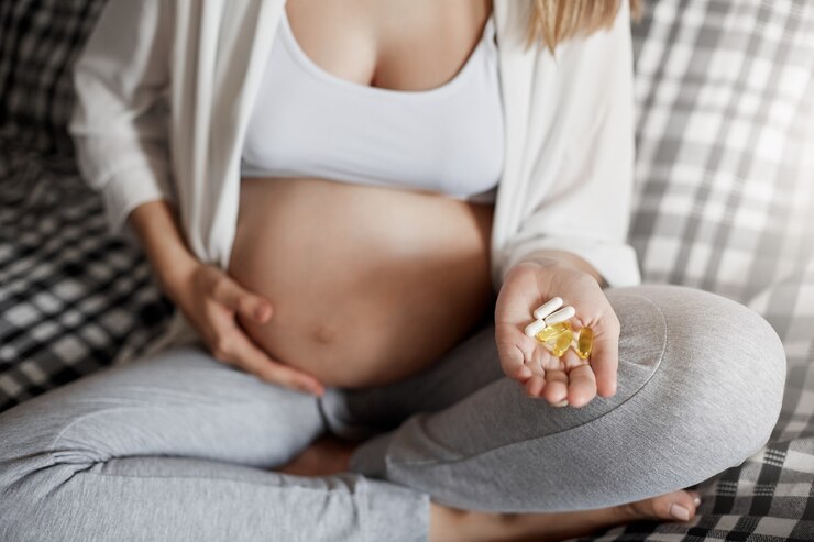 Pregnant woman holding pills on checkered bed, highlighting early pregnancy symptoms