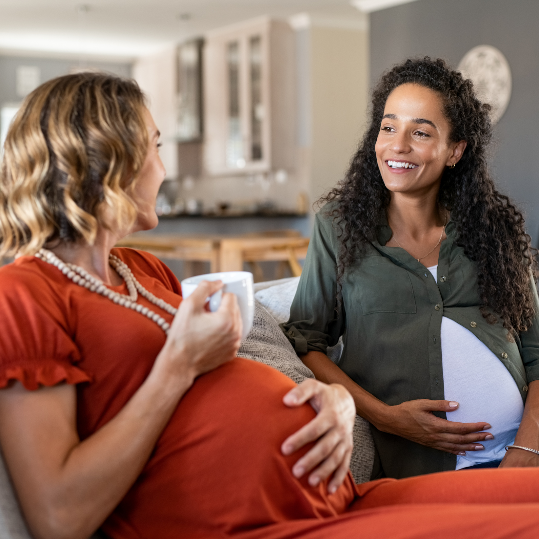 Two women chatting; iPhone nearby, woman in red dress, pregnant woman in green shirt.