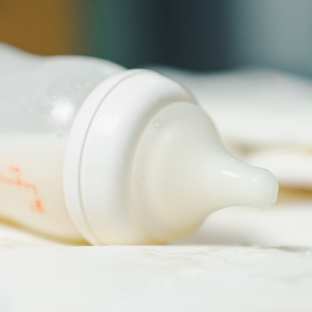 Baby bottle with white teat, blurred background emphasizing design.