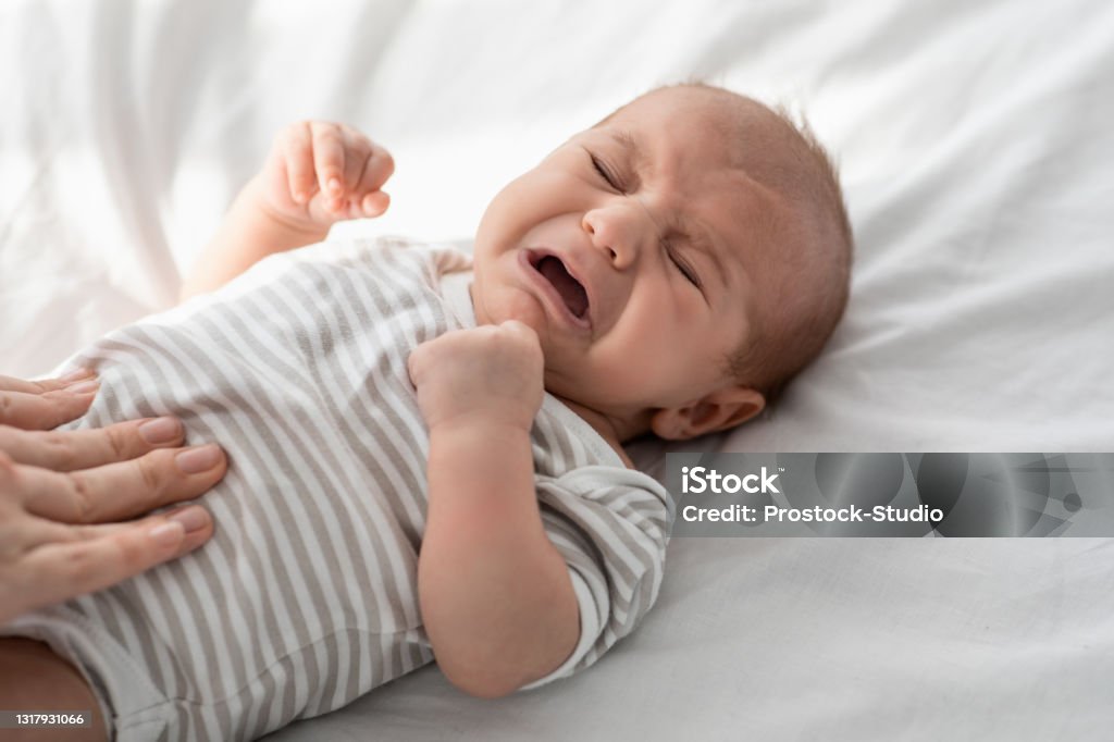 Crying baby lying in bed, comforted by adult, relating to milk consumption concerns