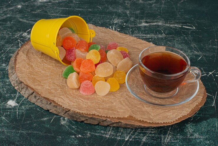 Yellow bucket of colorful gummy candies and a teacup on a rustic wooden table