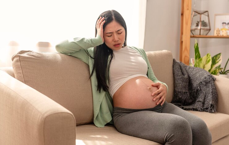 Woman in pain on beige couch, hands on stomach, early pregnancy guide focus