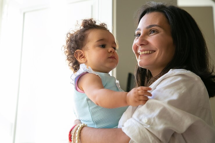 Woman smiling holding child wearing blue and white stripes, focus on nursing pads.