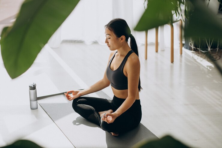 Young woman practicing mindfulness on yoga mat in serene, naturally lit room.