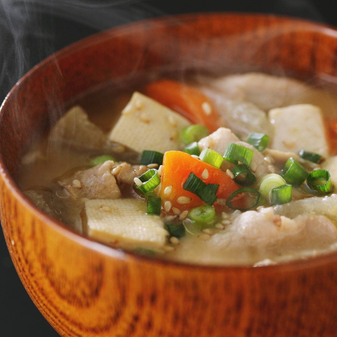 Rustic wooden bowl with steaming tofu soup, garnished with green onions and sesame seeds.