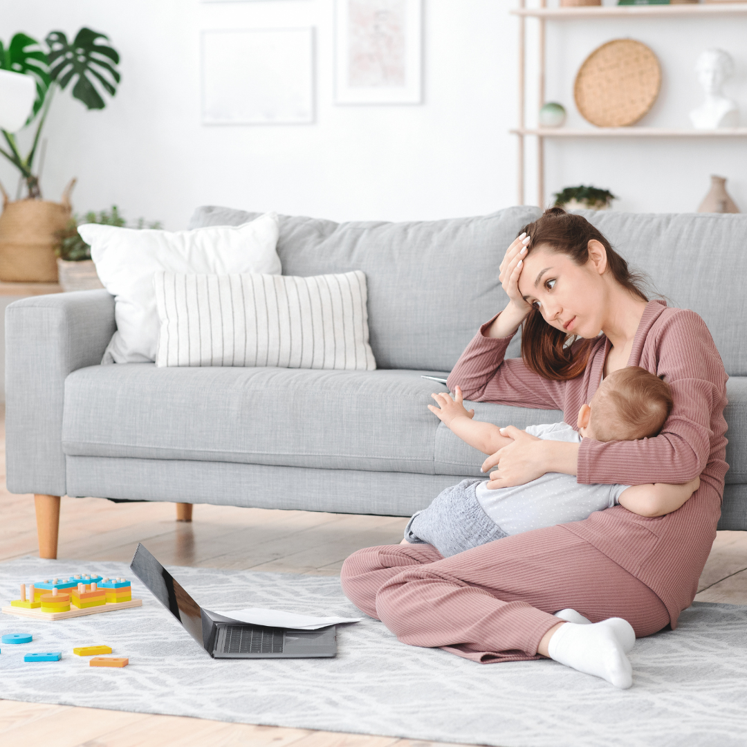 Woman holding baby with a laptop and smartphone on a gray couch in a cozy living room