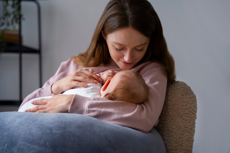 Woman cradling baby in white onesie on blue couch, conveying warmth and care. Baby formula.