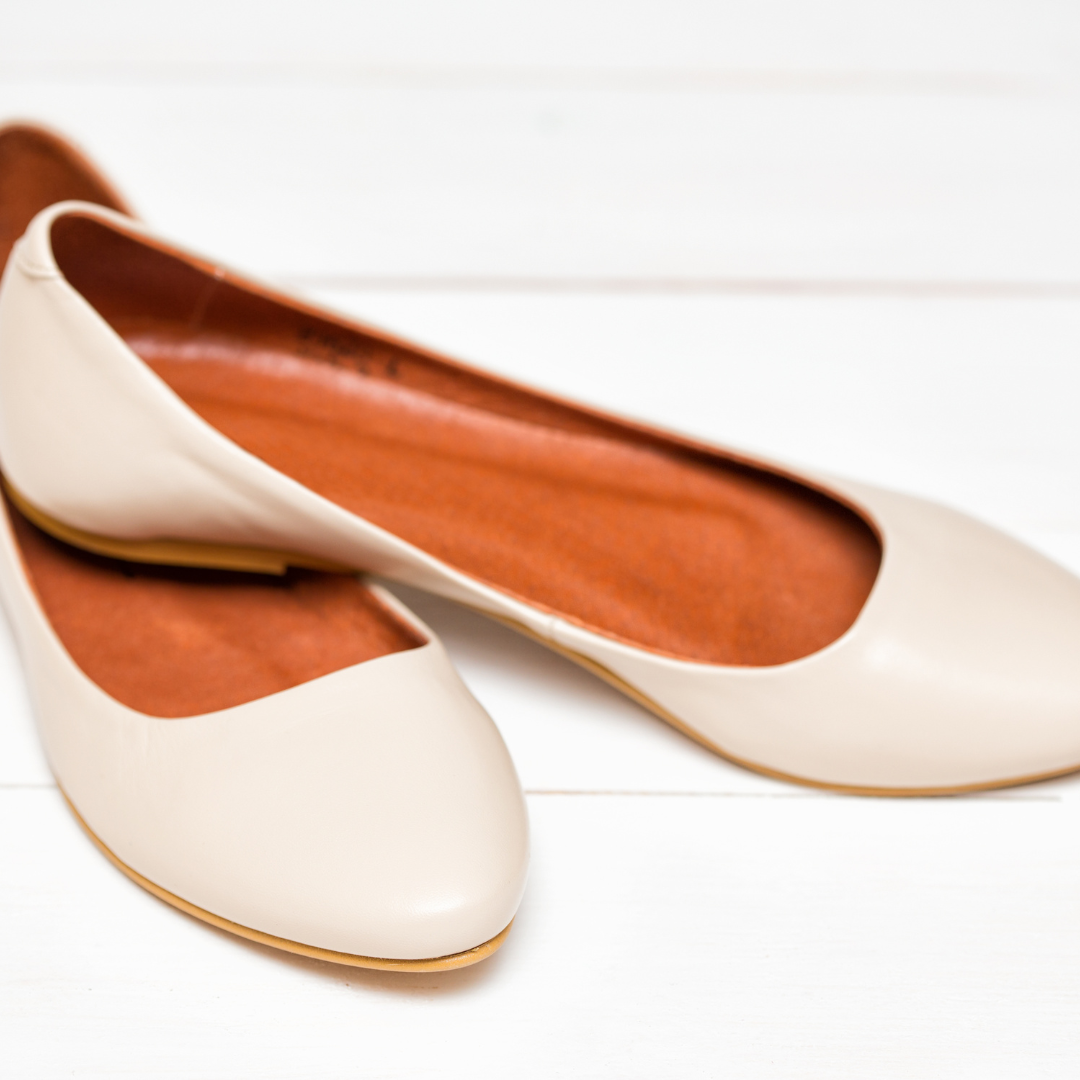 White flat shoes on white floor with vibrant orange insoles, diagonal positioning