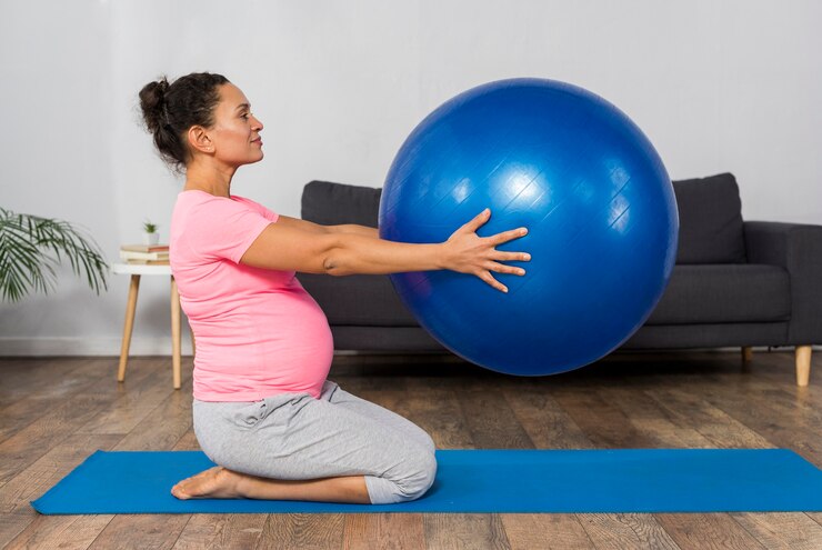 Woman doing prenatal exercise on blue mat with exercise ball in living room