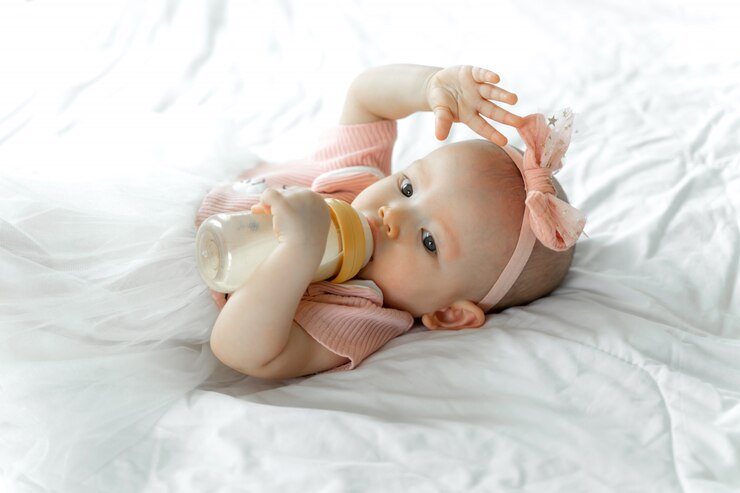 Baby in pink onesie with headband feeds on baby formula in soft white setting